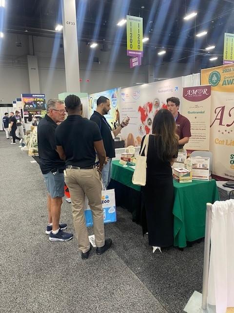 Show attendees gathered in the aisle talking with the AMOR FELINE team at the booth