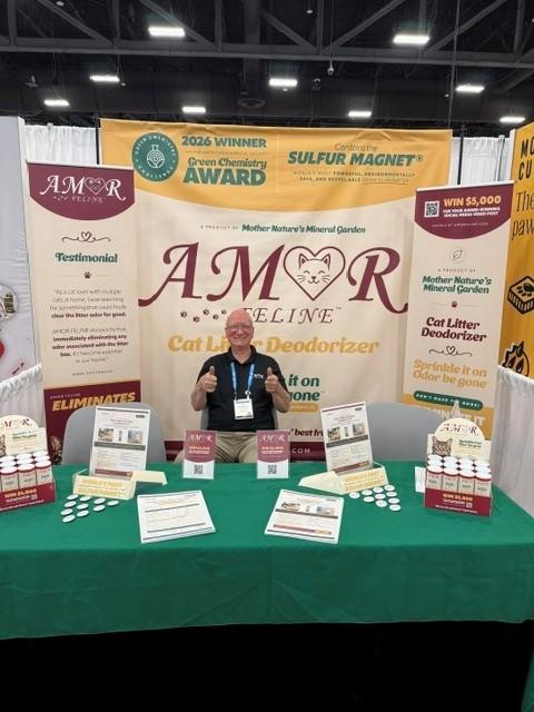 An AMOR FELINE team member giving a thumbs up behind the booth table stocked with product and literature
