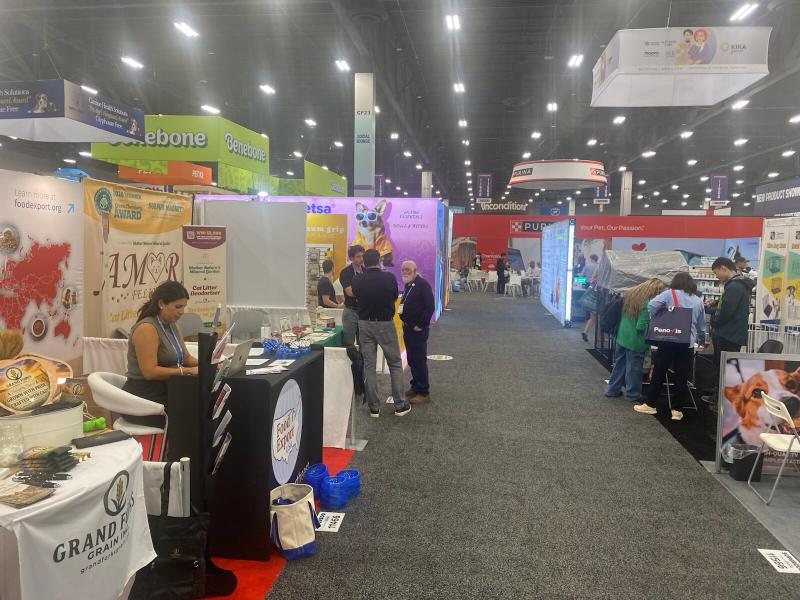 A wide view down a SUPERZOO exhibit aisle with the AMOR FELINE banner among the surrounding pet industry booths