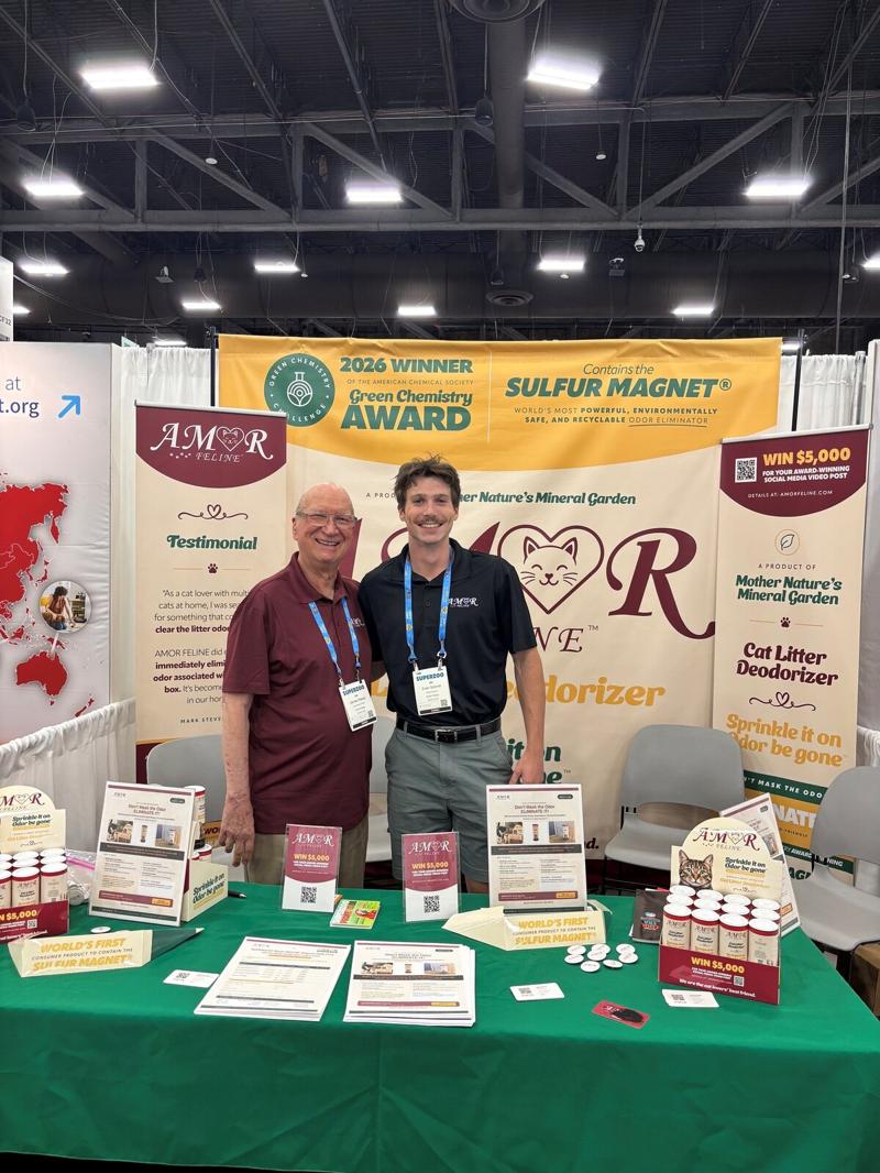 Two AMOR FELINE team members standing together behind the booth table under the Sulfur Magnet banner
